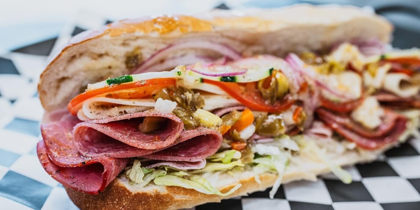 Italian sub stacked with salami, capicola and giardiniera on checkered paper